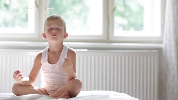 Счастливый расслабленный ребенок медитирует на белой кровати — стоковое видео