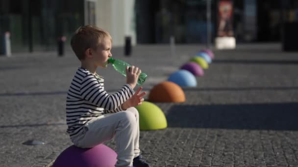 Gelukkig lachend dorst kleine jongen drinkwater op de gekleurde stenen in de stad — Stockvideo