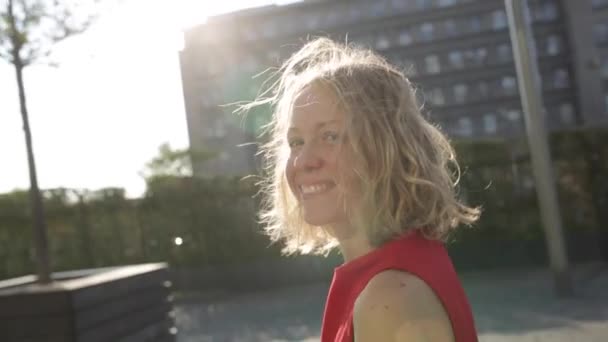 Jeune heureuse belle femme aux cheveux bouclés blonds souriant à la caméra marcher dans la ville — Video