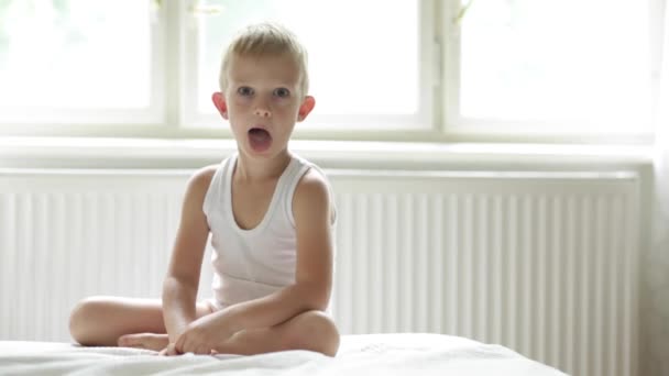 Счастливый расслабленный ребенок играет, шатается и шутит на белой кровати — стоковое видео