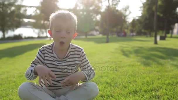 Lindo hermoso niño feliz sacudiendo la cabeza, sentado en la hierba — Vídeo de stock