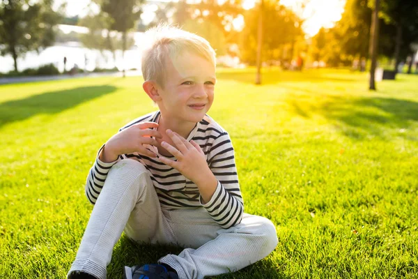 Søt, vakker, liten gutt som smiler og sitter på gress. – stockfoto