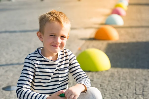 Bonito lindo feliz menino ruivo sorrindo, sentado em pedras coloridas Imagens De Bancos De Imagens
