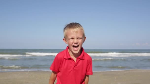 Χαρούμενος, ενθουσιασμένος αγοράκι γέλιο στην κάμερα στην παραλία κοντά στη θάλασσα — Αρχείο Βίντεο
