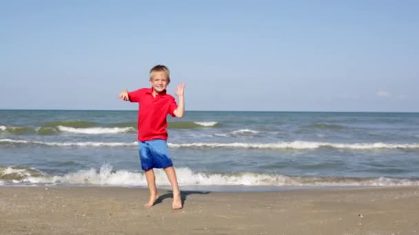Feliz niño saltando en la playa cerca del mar — Vídeos de Stock