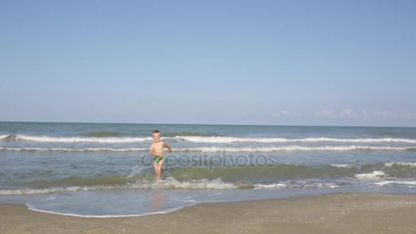 Glücklich lächelnder kleiner schöner Junge läuft aus dem Meerwasser an den Sandstrand — Stockvideo