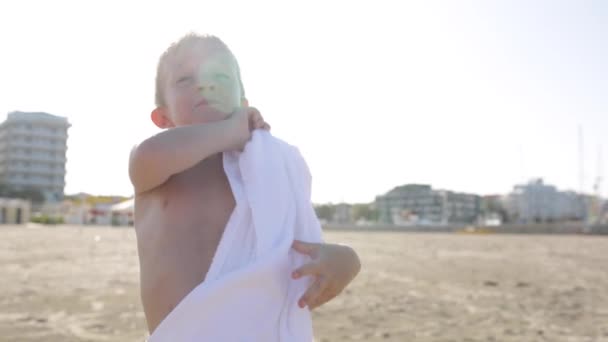 Szczęśliwy uśmiechający się mały chłopiec w biały ręcznik na plaży miasta morze żarty o kamery — Wideo stockowe