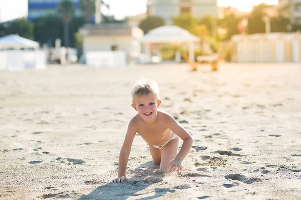 Szczęśliwy piękne dziecko uśmiechający się grać na piaszczystej plaży, patrząc na kamery — Zdjęcie stockowe