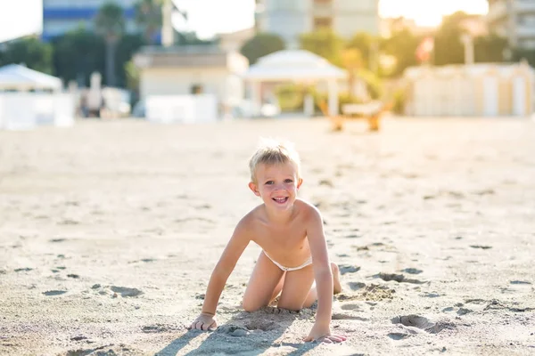 Gelukkig mooi lachende beetje jongen spelen op het zandstrand, camera kijken — Stockfoto