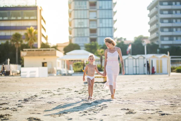 Happy beautiful young mom goes hand in hand with smiling cute child at city beach — Stock Photo, Image