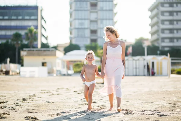 Feliz hermosa mamá va de la mano con sonriente lindo hijo en la playa — Foto de Stock