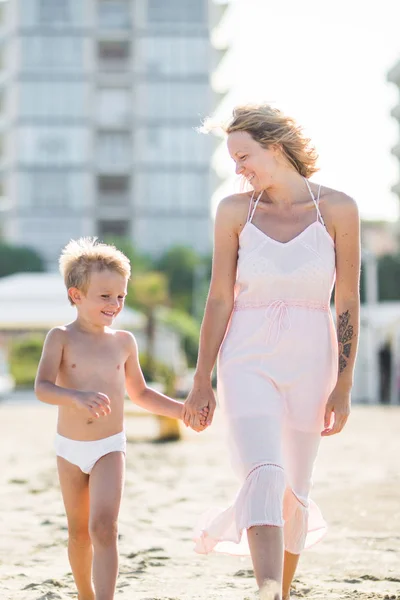 Feliz hermosa mamá va de la mano con el niño sonriente en la playa — Foto de Stock