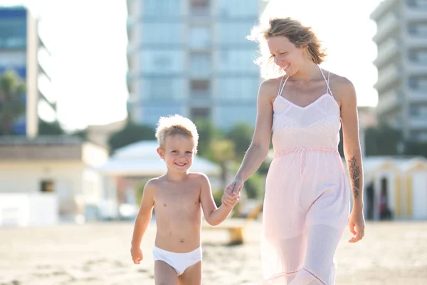 Gelukkig mooi moeder gaat hand in hand met lachende schattig kind op het strand van de stad — Stockfoto