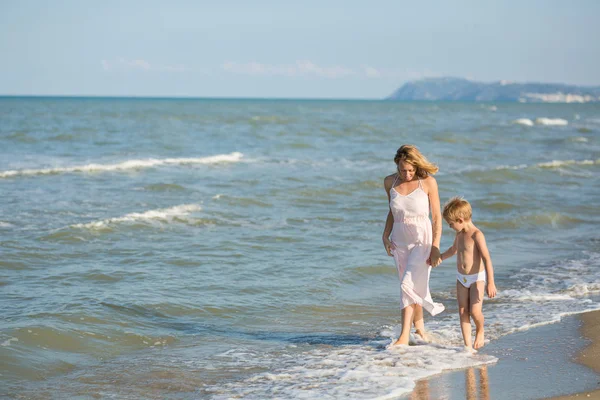 Gelukkig mooie jonge moeder en kind lopen en praten langs de zee — Stockfoto