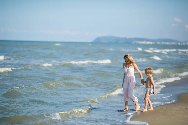 Glada vackra mamma och barn vandra längs en strand vid havet — Stockfoto