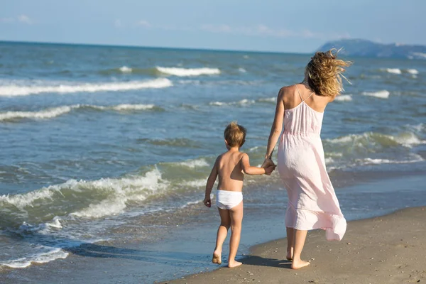 Szczęśliwy, że piękna mama i dziecko chodzić daleko wzdłuż plaży morza, fale i wiatr — Zdjęcie stockowe