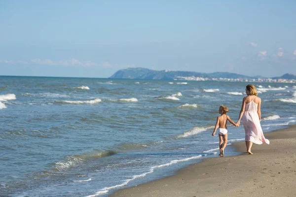 Szczęśliwy piękna młoda Mama i dziecko chodzenie daleko wzdłuż brzegu morza-miejsce — Zdjęcie stockowe