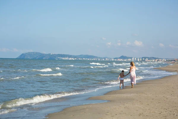 Gelukkig mooie jonge moeder en kind ver wandelen langs de zee-strand — Stockfoto