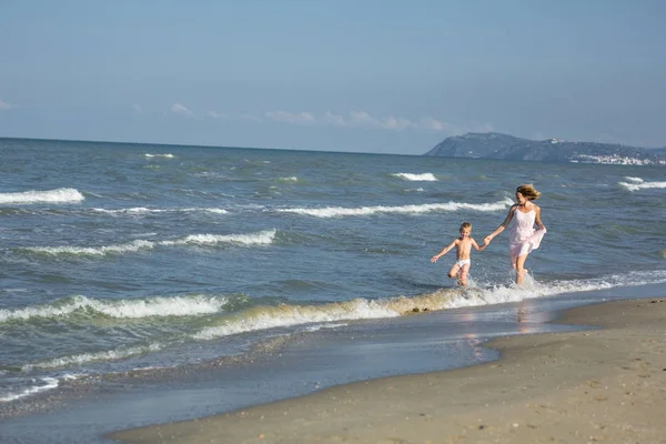 Szczęśliwy piękna mama i dziecko, które biegną wzdłuż brzegu morza-miejsce — Zdjęcie stockowe