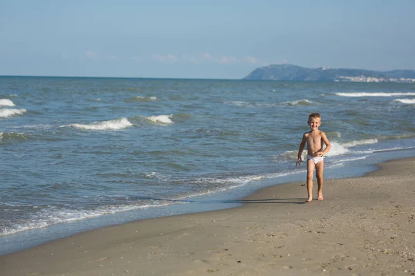 Gelukkig glimlachend jongetje loopt langs de zee-strand — Stockfoto