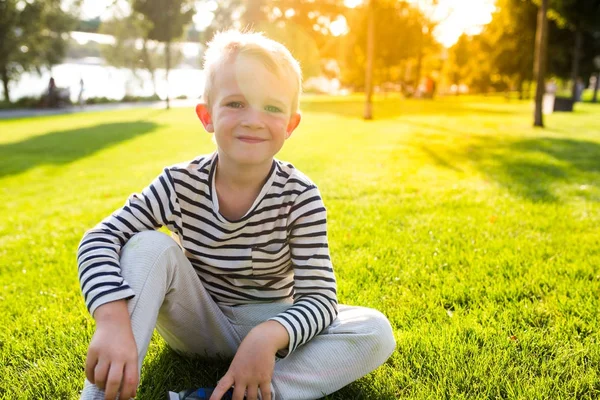 Vakker, smilende liten gutt sitter på gresset og ser på kamera – stockfoto