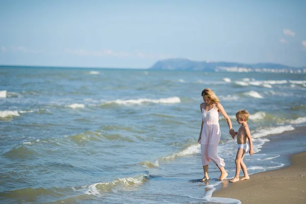 Happy beautiful mom and child walking along the sea beach Stock Image