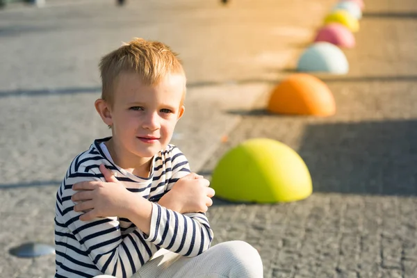 Beautiful happy little boy sitting on colored stones, look at camera Stock Picture