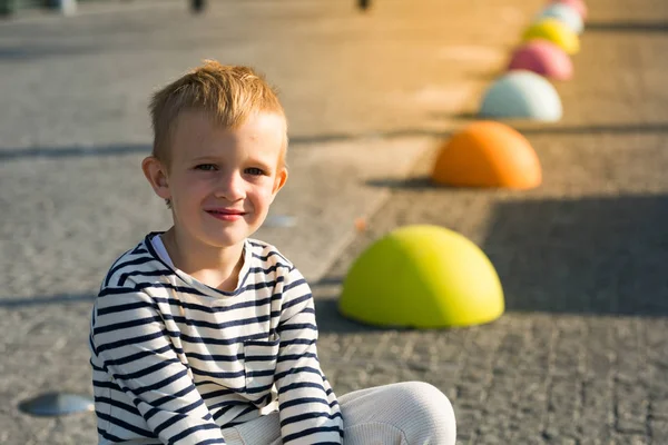Kameraya bakarak renkli taşlar üzerinde oturan güzel mutlu bir çocuk - Stok İmaj