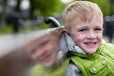 Mutlu gülümseyen yakışıklı sarışın çocuk kameraya bakarak bir bankta oturmuş