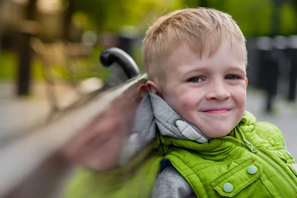 Happy smiling handsome blonde boy sitting on a bench looking at camera — Stock Photo, Image