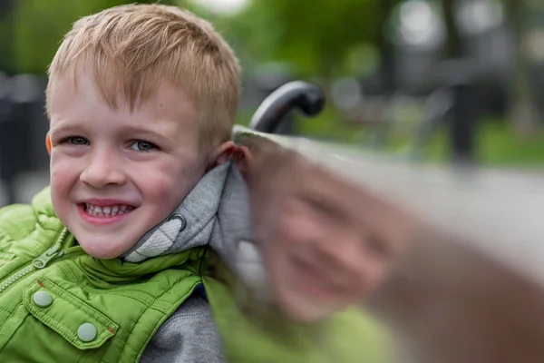 快乐的微笑英俊的金发男孩坐在长凳上看着相机 — 图库照片