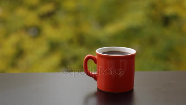 Taza roja de café oscuro sabroso caliente en una mesa de café de madera al aire libre, fondo de otoño — Vídeos de Stock