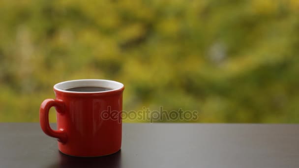 Taza roja de bebida caliente sabrosa en una mesa de café de madera al aire libre, fondo de otoño — Vídeos de Stock