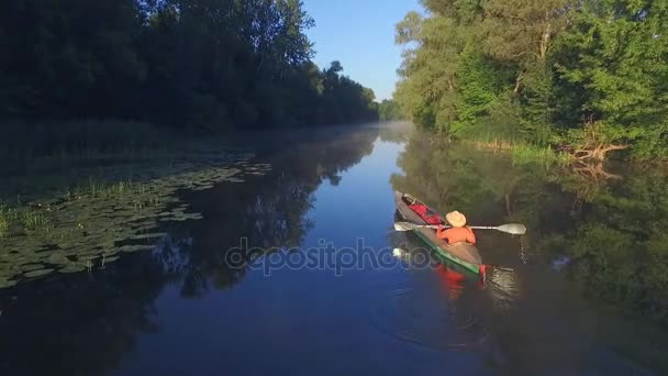 En kvinnlig figur i en båt seglar på en lugn flod — Stockvideo