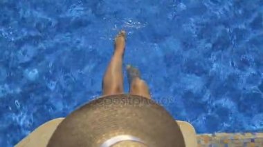 Bir kız havuz başında mavi su bacaklarda oturur.