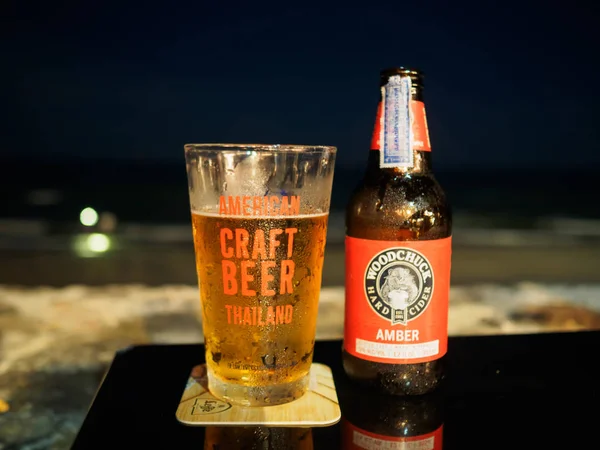 HuaHin, Tailandia 9 de abril de 2017: Botella de Woodchuck Cerveza ámbar y vaso de cerveza artesanal estadounidense sobre la mesa en HuaHin Beach durante la noche . — Foto de Stock