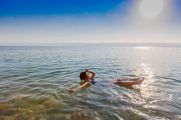 Ragazza galleggiante sulla superficie del Mar Morto, Giordania, godere la sua vacanza durante il tramonto in estate . — Foto Stock