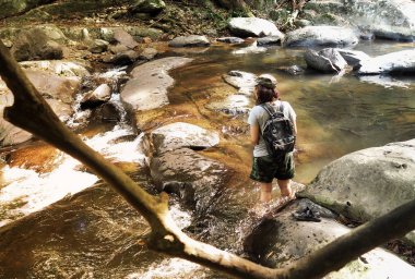 Kız cascade, su akışı arasında güneş shini sırasında yürüyüş ile sırt çantası ve trekking gezi, fotoğraf makinesi
