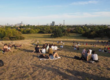 LONDON, İngiltere - CIRCA SEPTEMBER 2019: Regent 's Park' ın kuzeyindeki Primrose Hill 'de insanlar gün batımında Londra ufuk çizgisine bakıyor