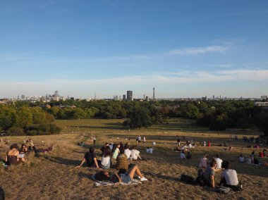 LONDON, İngiltere - CIRCA SEPTEMBER 2019: Regent 's Park' ın kuzeyindeki Primrose Hill 'de insanlar gün batımında Londra ufuk çizgisine bakıyor