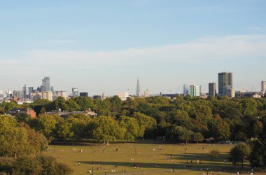 LONDON, İngiltere - CIRCA SEPTEMBER 2019: Regent 's Park' ın kuzeyindeki Primrose Hill 'de insanlar gün batımında Londra ufuk çizgisine bakıyor