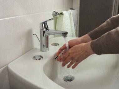 Tanınmayan bir adam sağlık güvenliği için evde ellerini dikkatlice yıkıyor.