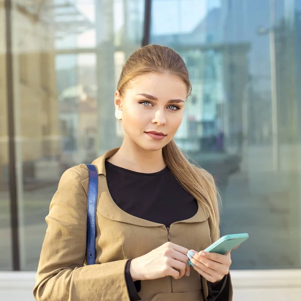 Portret van mooie jonge vrouw met behulp van haar mobiele telefoon in de straat op voorjaar — Stockfoto
