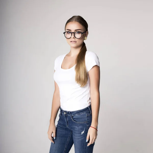 Atractiva rubia con gafas mirando hacia otro lado, contra la foto gris. mujer en blanco camiseta blanca —  Fotos de Stock