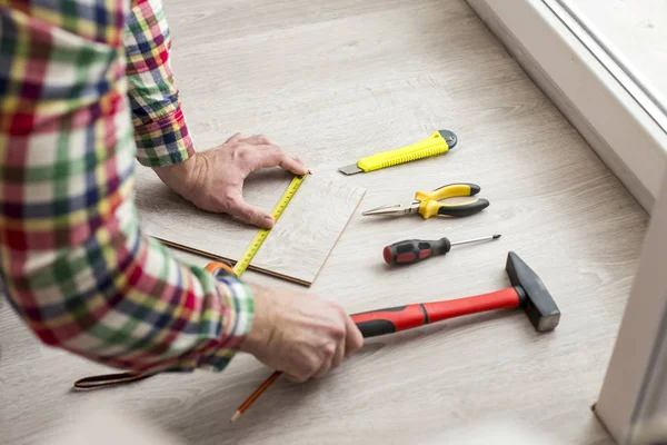 Trabalhador coloca laminado. Na imagem as mãos de um homem e diferentes instrumentos — Fotografia de Stock