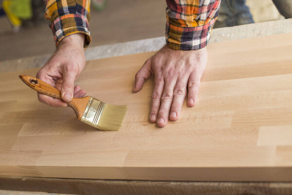 Handyman varnishing pine wooden planks in patio outside the new house