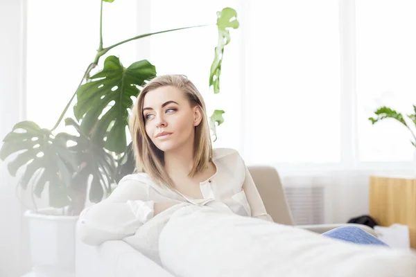 Junge blonde Frau ruht sich zu Hause auf einem Sofa im Wohnzimmer aus lizenzfreie Stockbilder