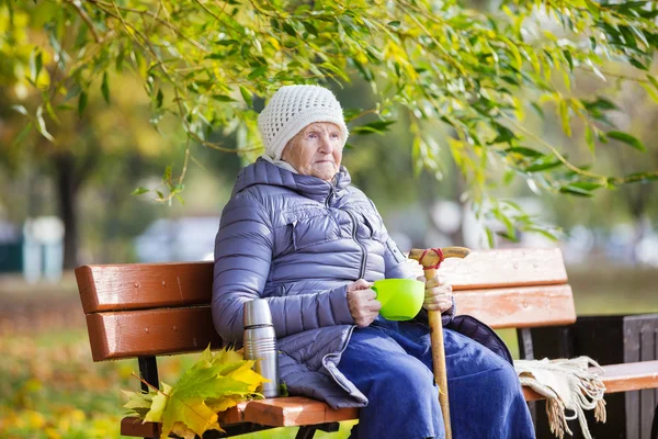 Seniorin trinkt heißen Tee im Herbstpark — Stockfoto