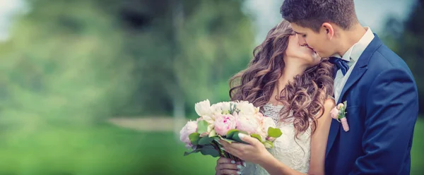 Bruid en bruidegom kussen in park — Stockfoto