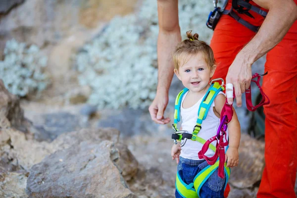 Young man putting climbing gear on his little daughter